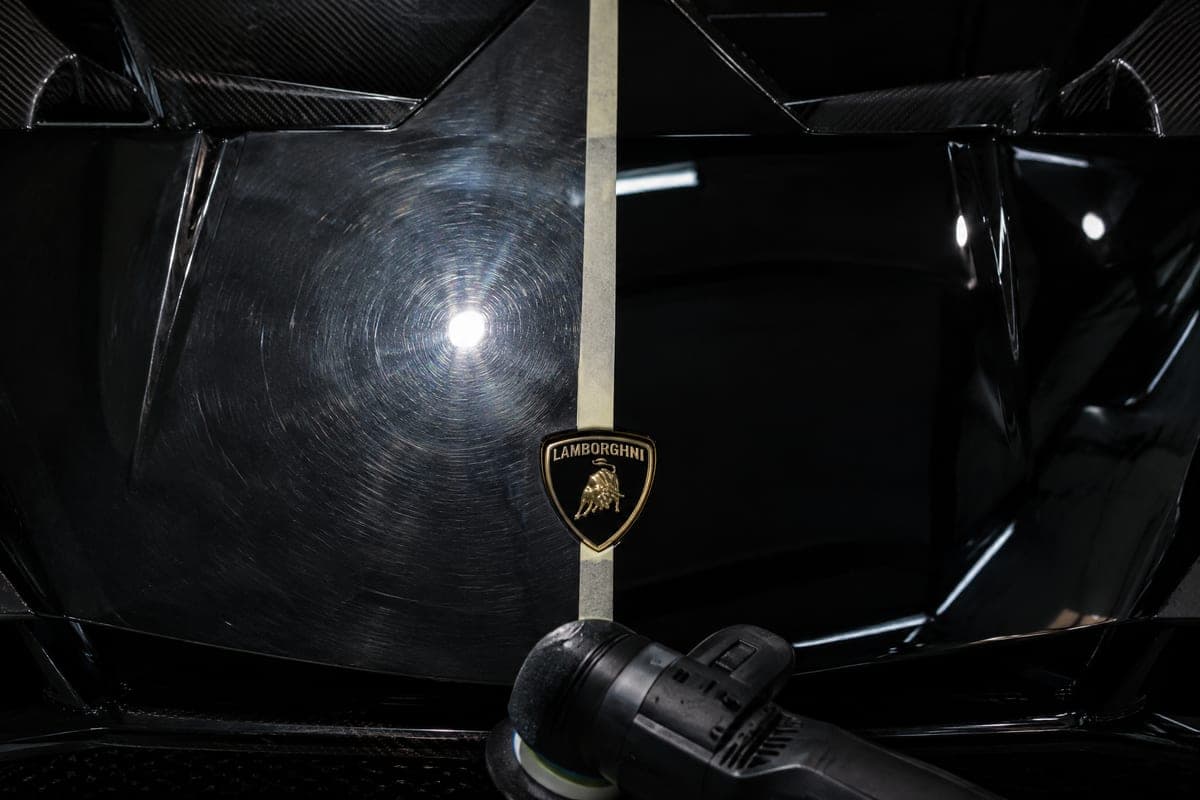 Black Lamborghini paint split down the middle: swirl marks on one side, a perfect reflection on the other